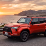 Red 2026 Toyota RAV4 PHEV parked on a coastal highway overlooking the ocean during a golden sunset.