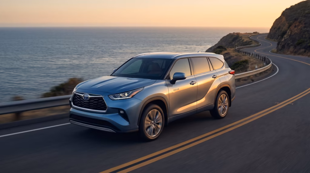 Blue Toyota Highlander Hybrid SUV driving along a scenic coastal highway during a sunset.