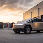 Stainless-steel Tesla Cyberbeast electric pickup truck charging at a Tesla Supercharger station beside a modern building at sunset.
