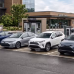 Best hybrid vehicles of 2026 including a hatchback, sedan, and compact SUVs parked at a modern automotive plaza featuring fuel pumps and electric chargers.